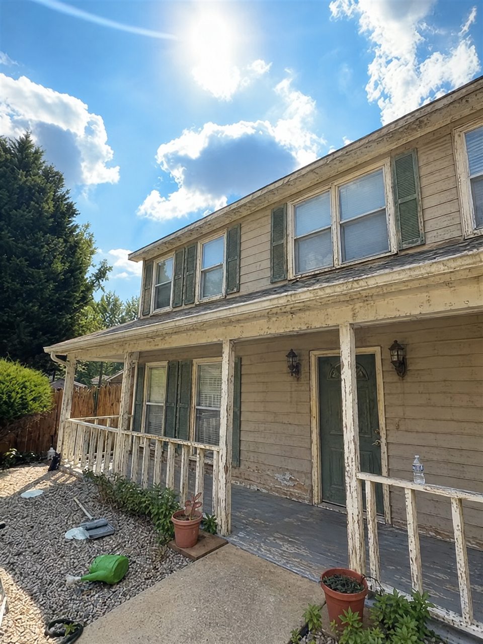 Two-story house with faded tan siding and peeling porch before painting
